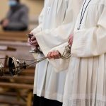 A minister in a white robe holds a censer during Holy Mass