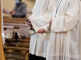 A minister in a white robe holds a censer during Holy Mass