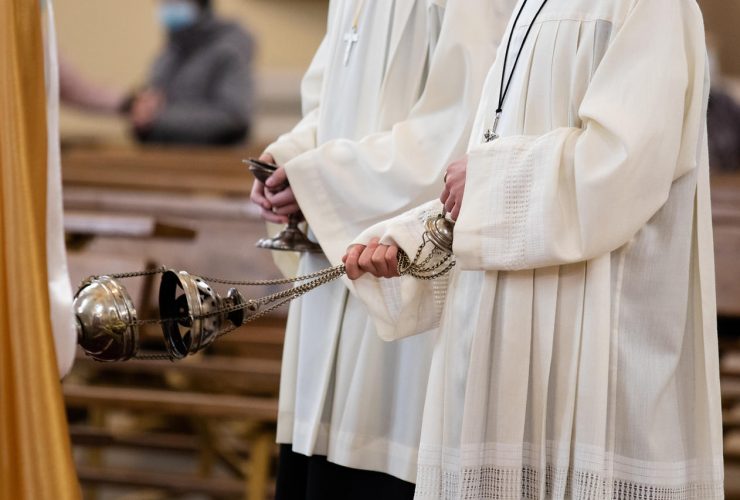 A minister in a white robe holds a censer during Holy Mass