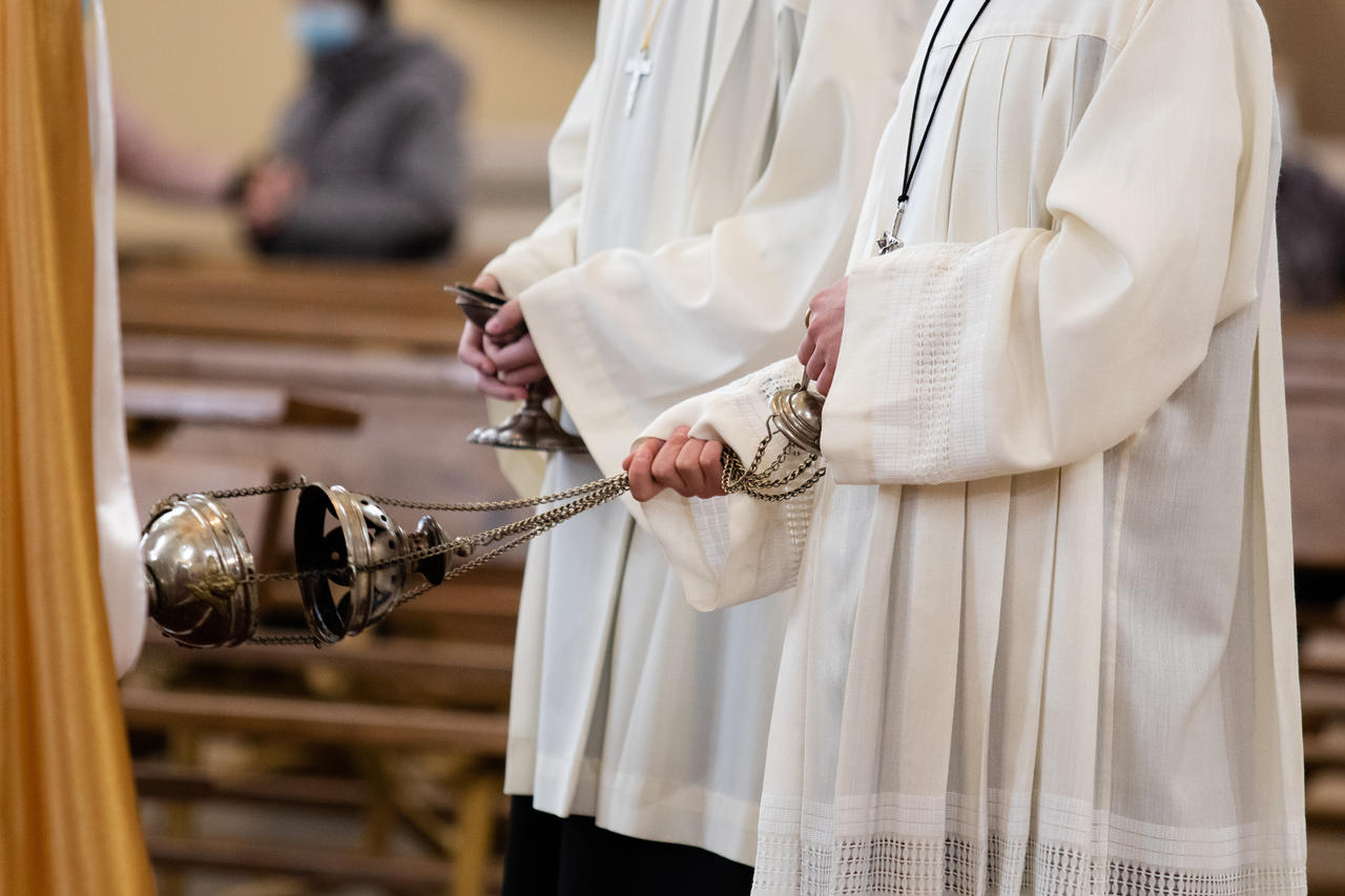 A minister in a white robe holds a censer during Holy Mass