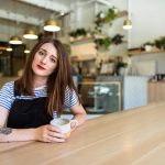 Woman in black and white shirt under underalls with coffee