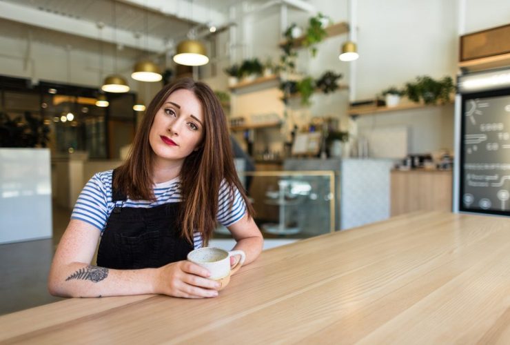 Woman in black and white shirt under underalls with coffee